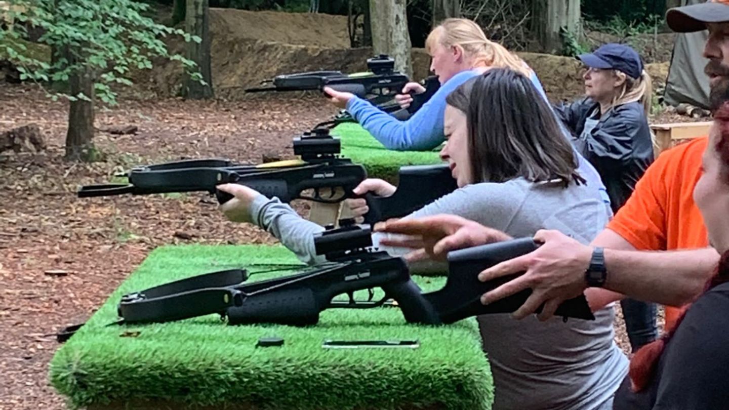 People aiming rifles at a shooting range in a forest setting.