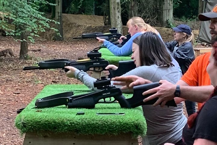 People aiming rifles at a shooting range in a forest setting.