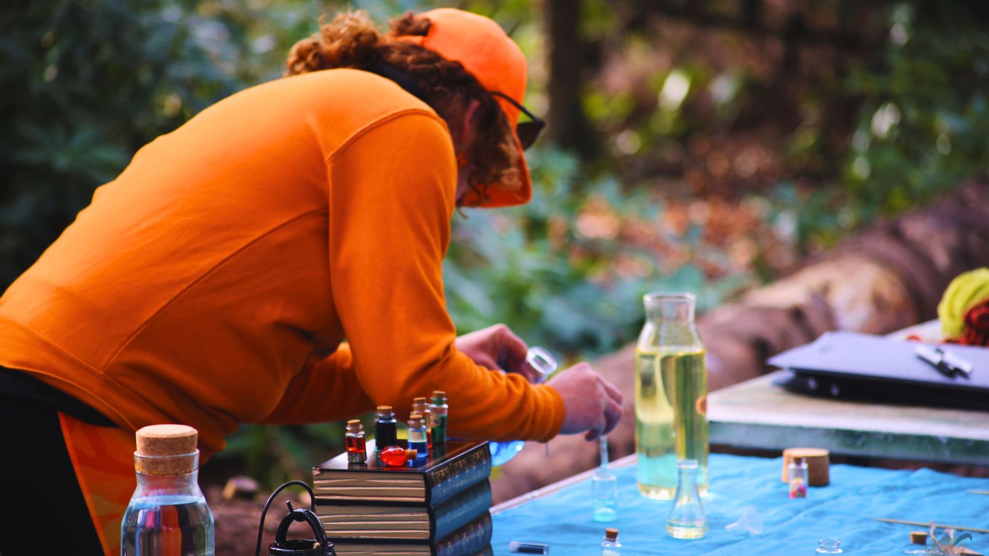 Person in orange attire working with small bottles on an outdoor table.