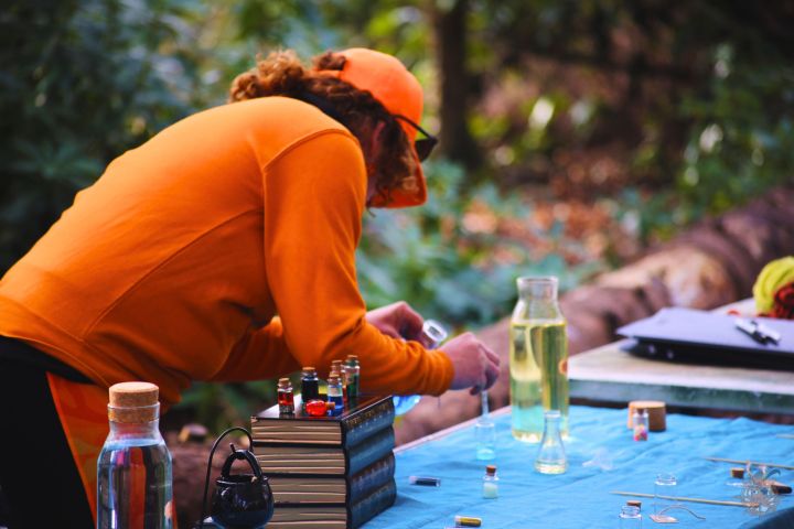 Person in orange attire working with small bottles on an outdoor table.