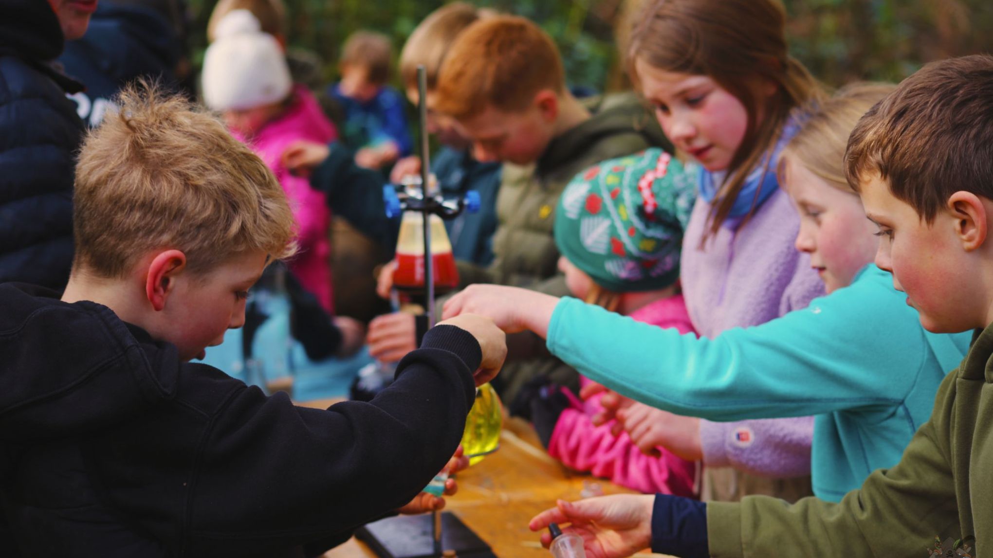 Children engaged in outdoor science experiments with test tubes and beakers on a table.