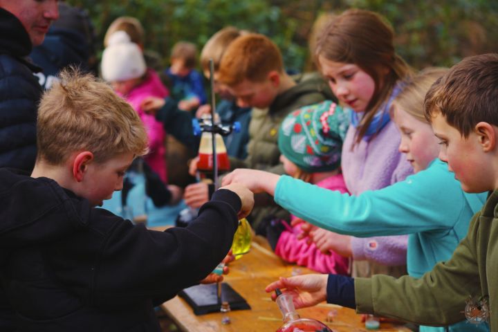 Children engaged in outdoor science experiments with test tubes and beakers on a table.