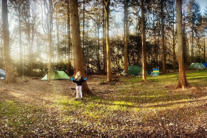 Child playing in a wooded campsite with several tents on a sunny day.