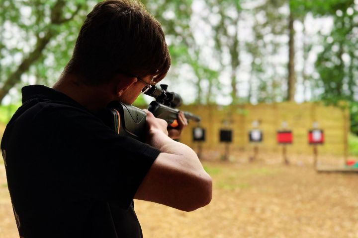 Person aiming a rifle at distant targets in an outdoor range.