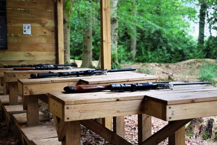 Rifles on wooden benches in an outdoor wooded area.