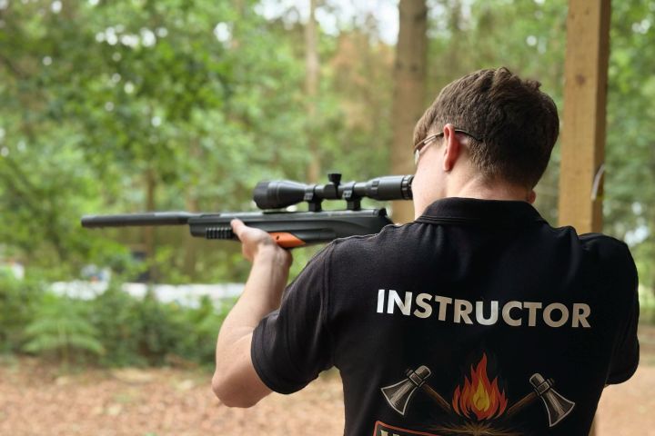 Instructor aiming a rifle in a wooded area.