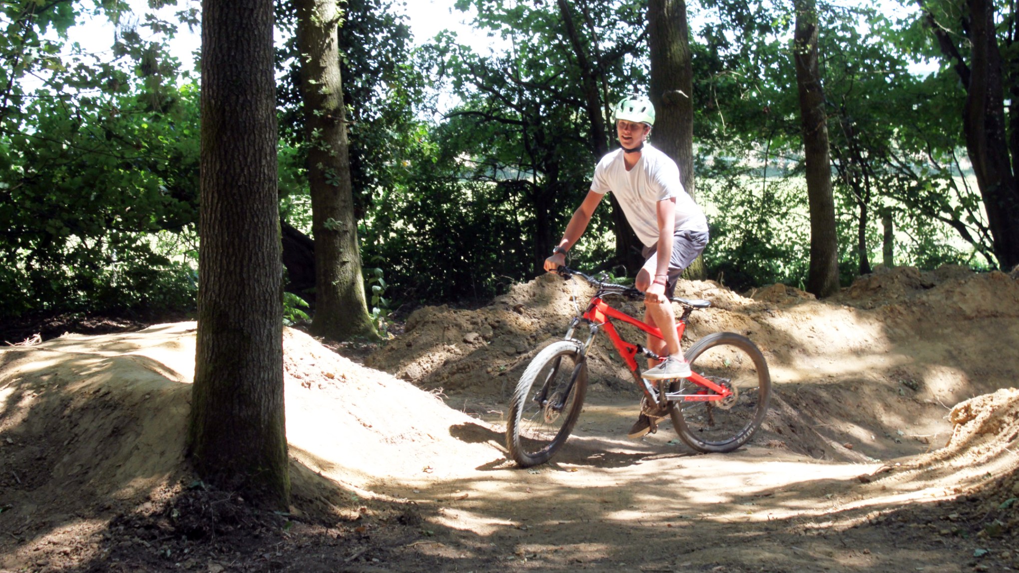 Person riding a red mountain bike on a dirt trail in a wooded area.