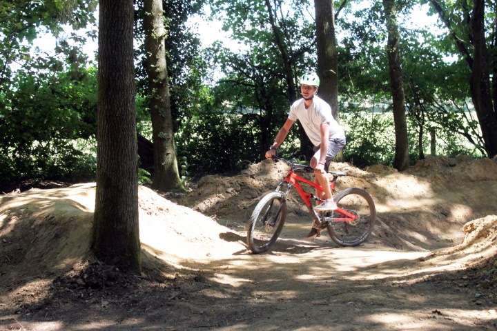Person riding a red mountain bike on a dirt trail in a wooded area.