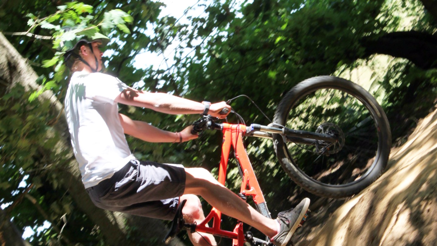 Person on a red mountain bike biking uphill in a forested area.