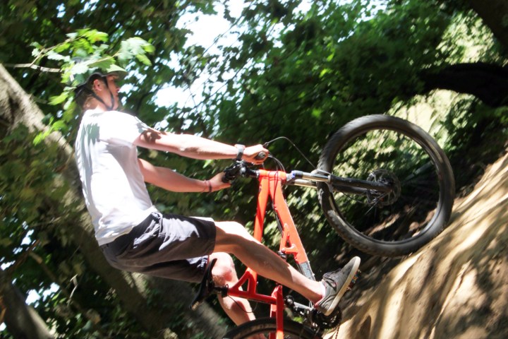 Person on a red mountain bike biking uphill in a forested area.