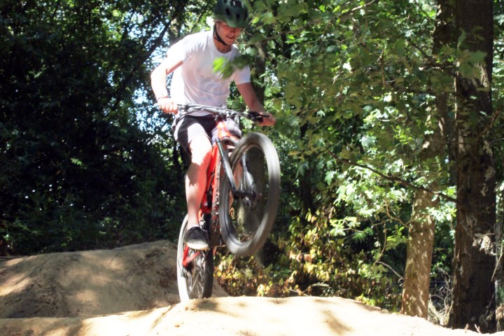 Cyclist performing a jump on a dirt trail in the forest.