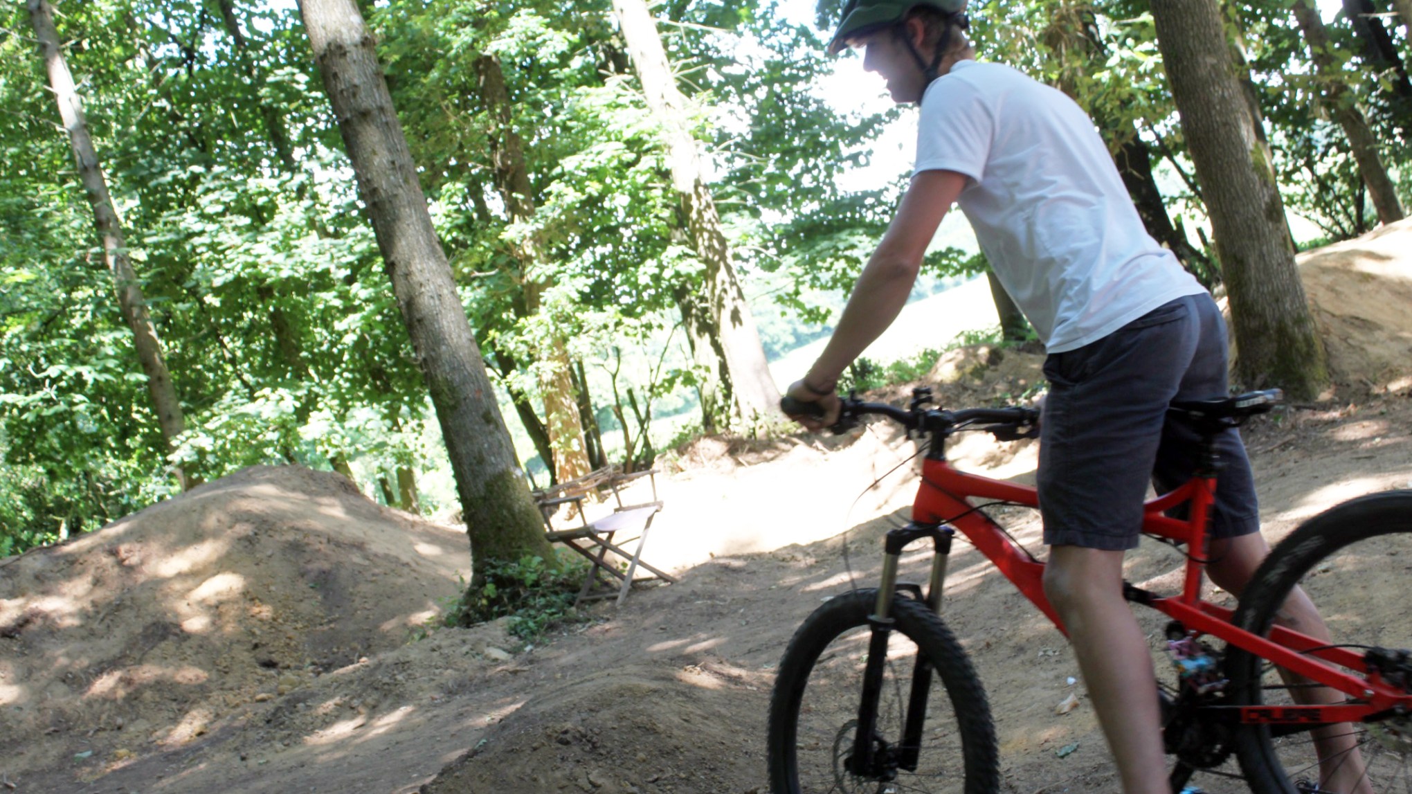 Person wearing a helmet rides a red mountain bike on a dirt trail in a wooded area.
