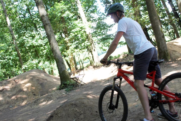 Person wearing a helmet rides a red mountain bike on a dirt trail in a wooded area.