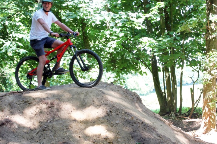 Person on a mountain bike atop a dirt mound in a forest.