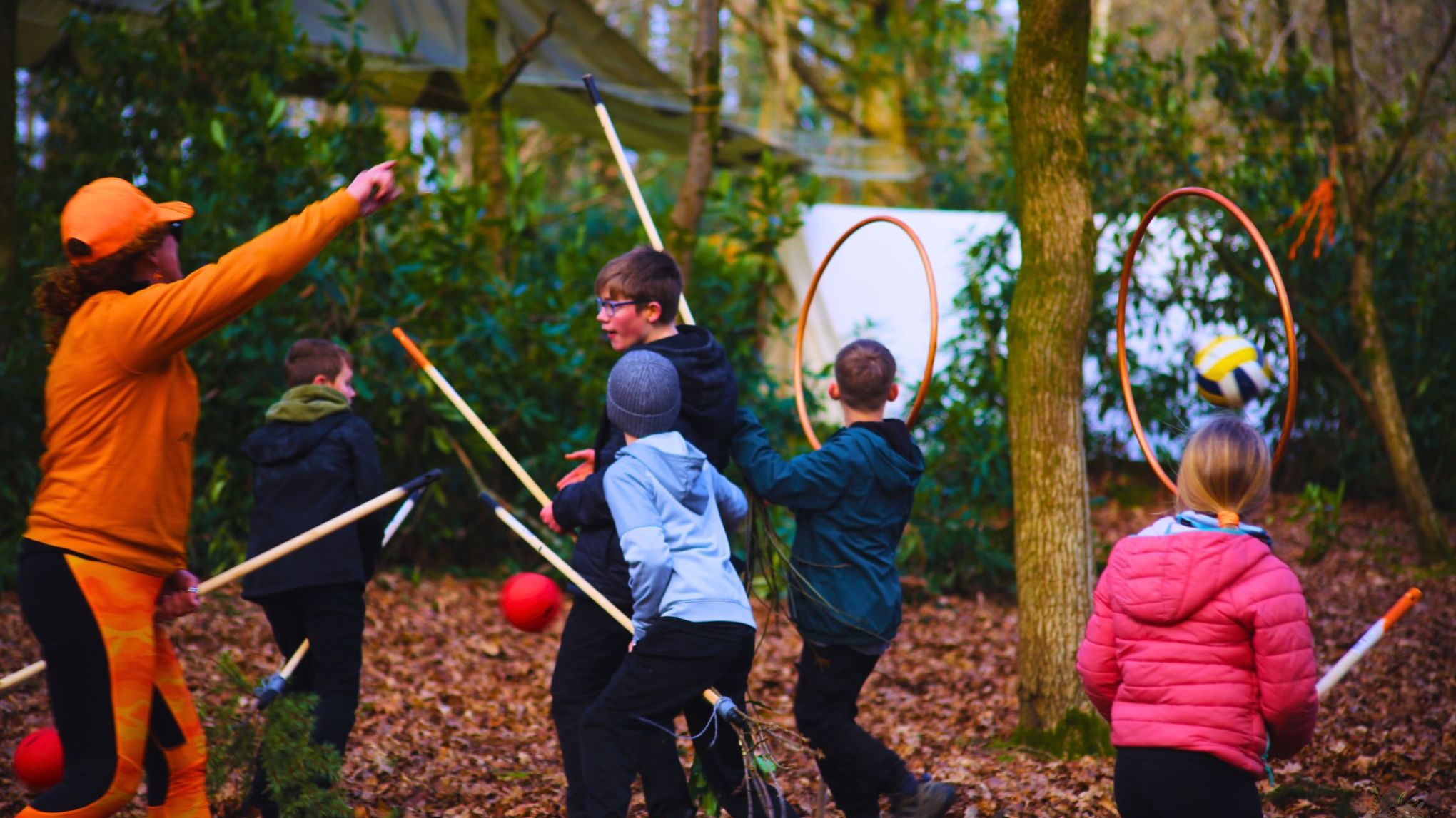 Children playing a game with sticks and hoops in a forest setting.