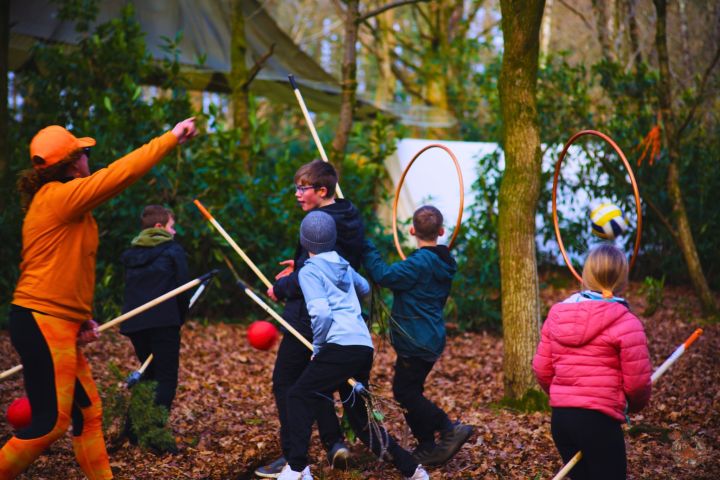 Children playing a game with sticks and hoops in a forest setting.