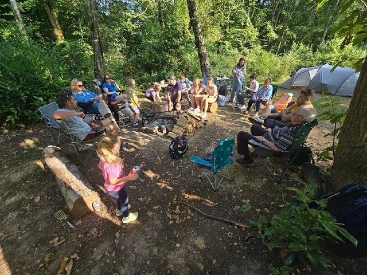 Group of people sitting in a circle in a forest campsite.