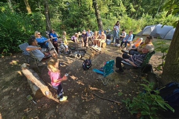 Group of people sitting in a circle in a forest campsite.
